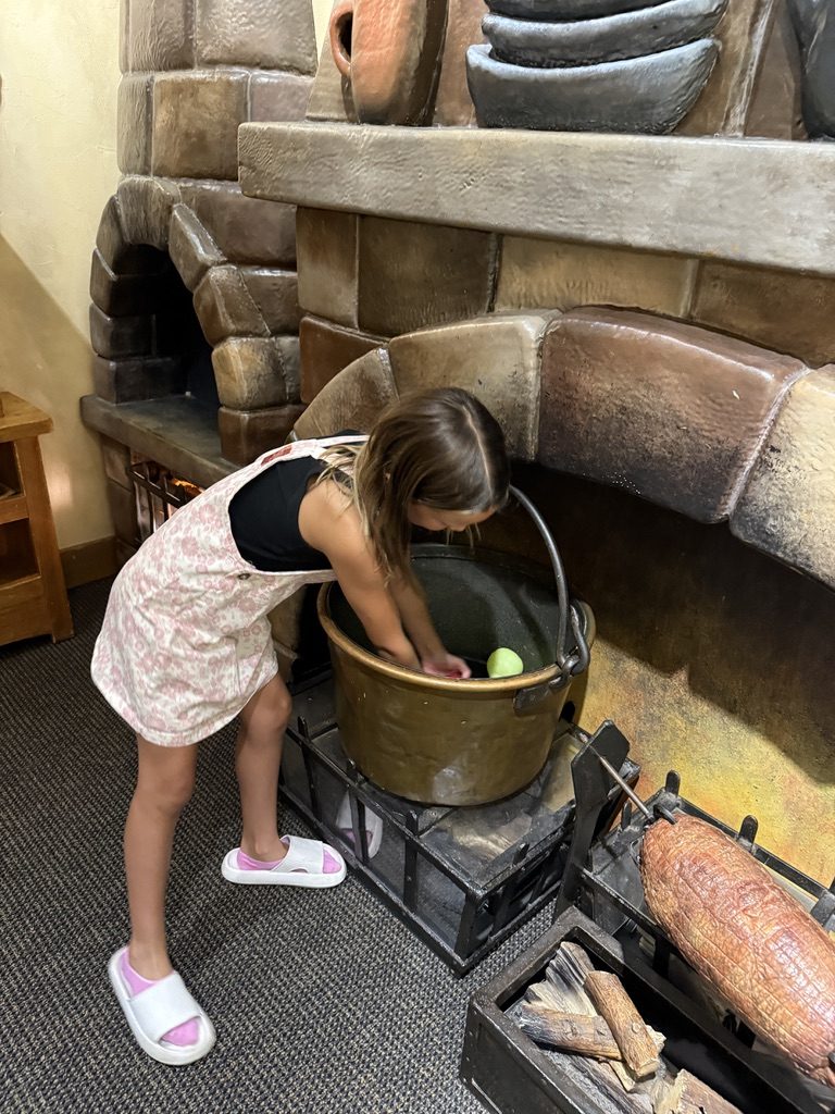 A girl leaning over a cauldron at a stone fireplace display