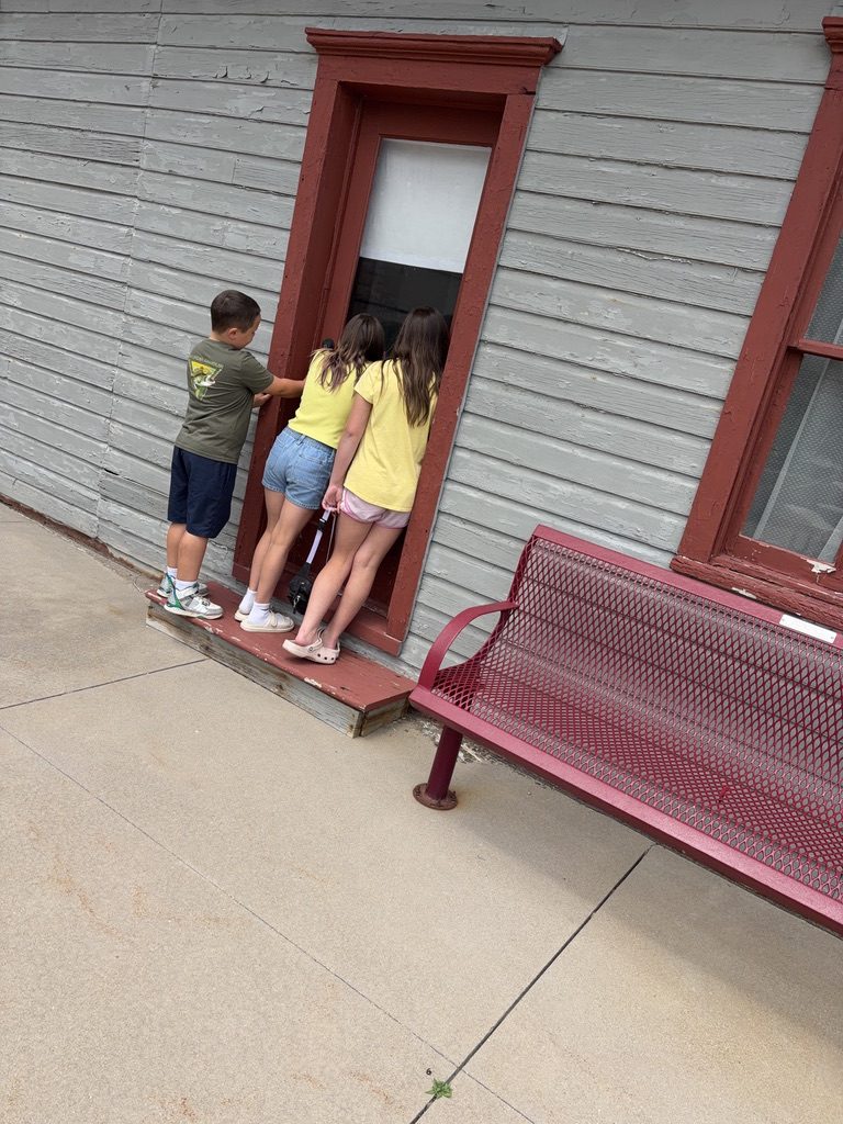 Three children seen from behind, peeking into the window of a historic Czech home display at the museum